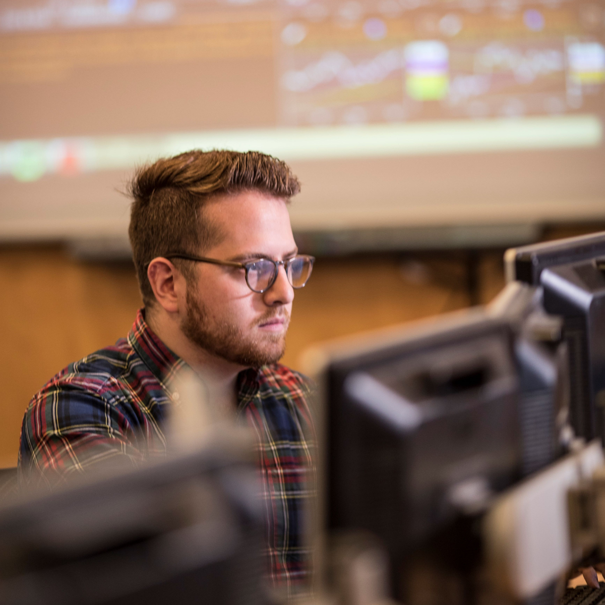 A student focuses on multiple computer screens displaying data and charts