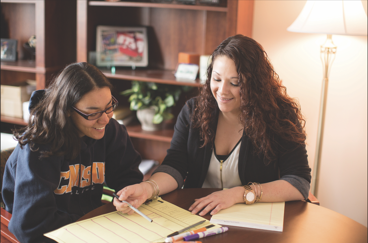 Two women sit at a table reviewing notes together