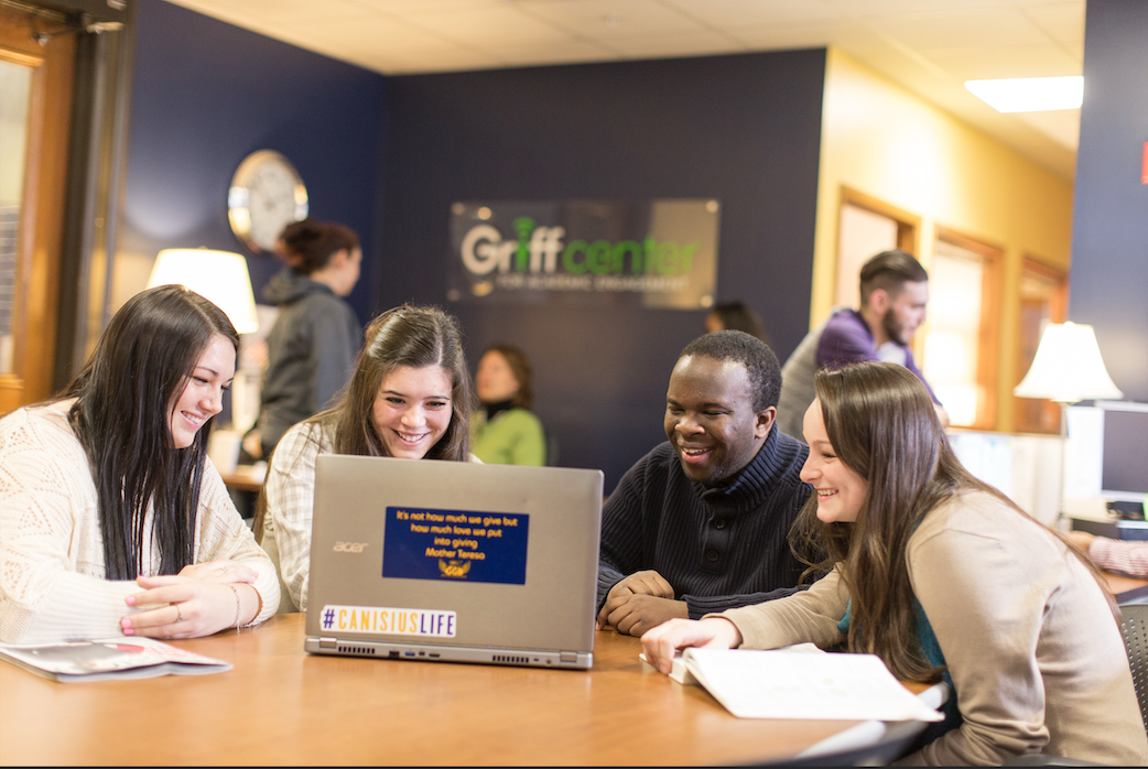 Four students sit together at a table while looking at a laptop in the Griff Center at Canisius University.