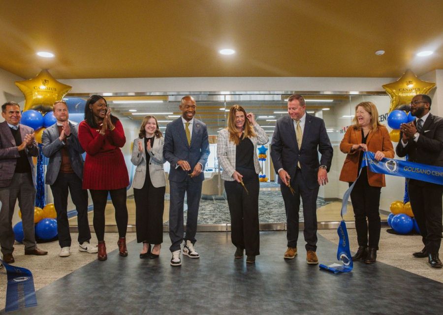 A group of people standing in a line smiling during a ribbon cutting ceremony/ 