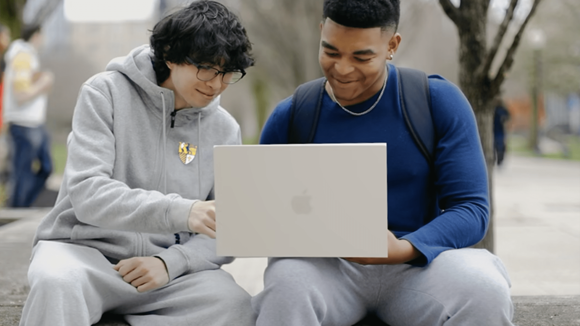 2 students sitting outside on a college campus looking at a laptop together