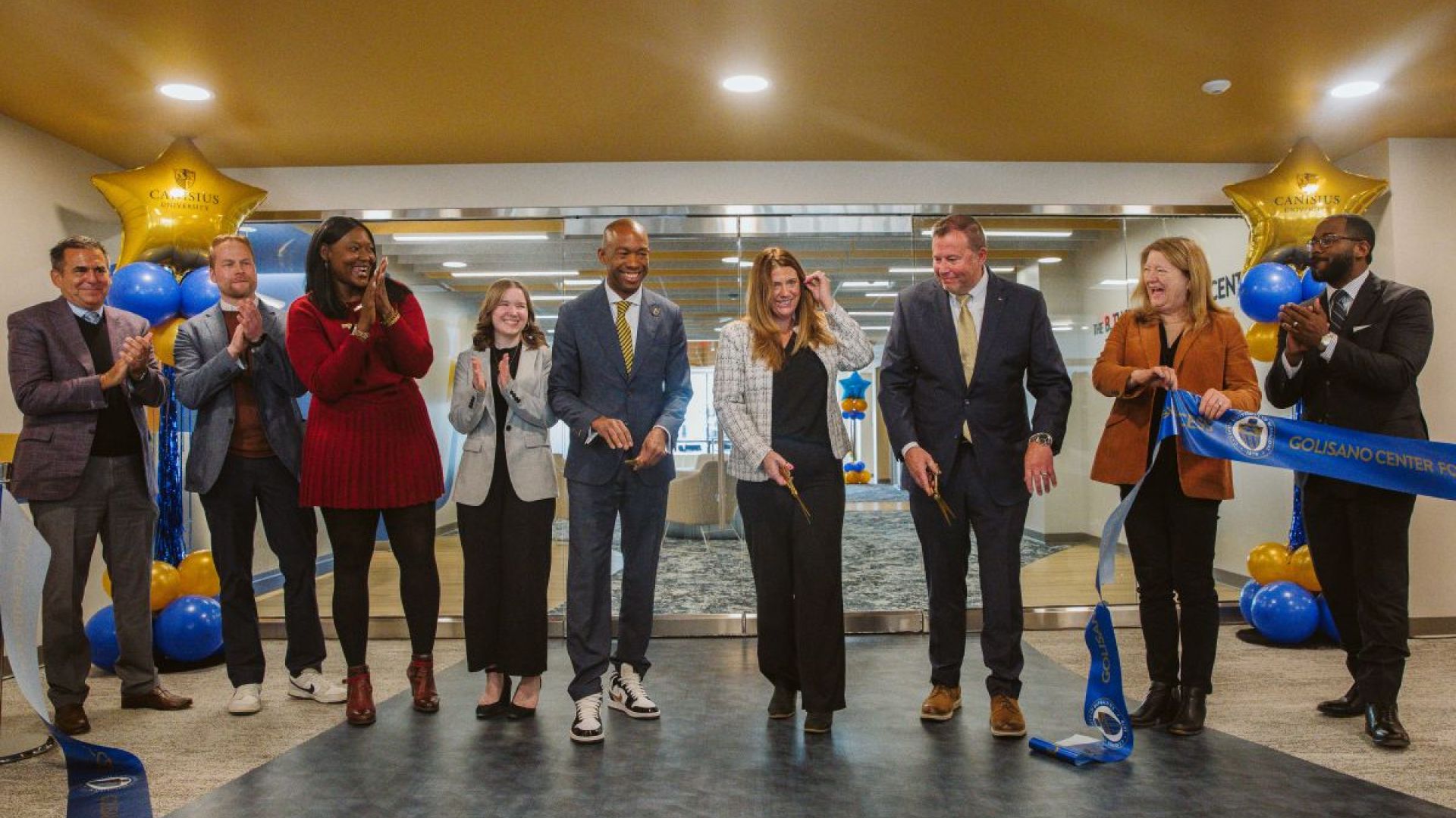 A group of people standing in a line smiling during a ribbon cutting ceremony/ 