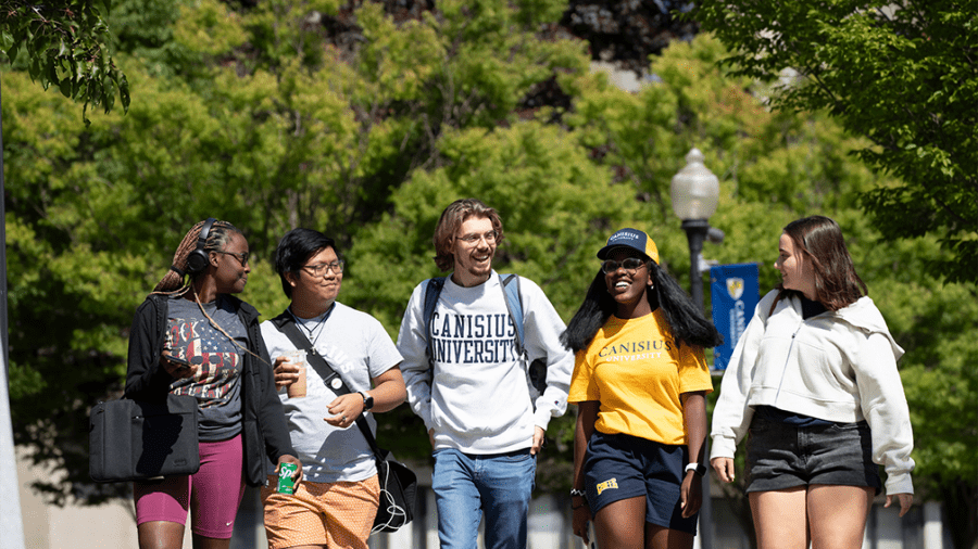 students walking across a college campus quad area in the summer discussing a topic as a group