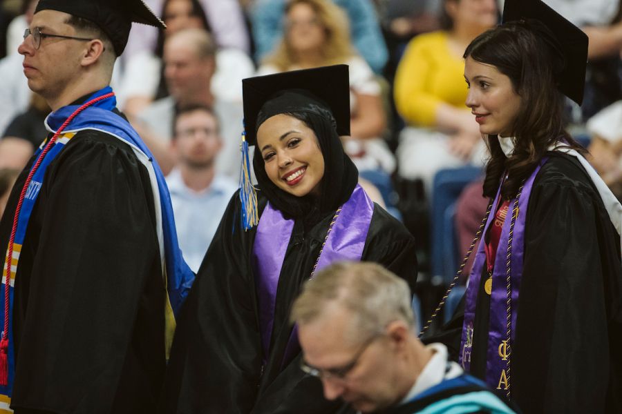 Student at a college graduation smiling in a cap and gown while in line