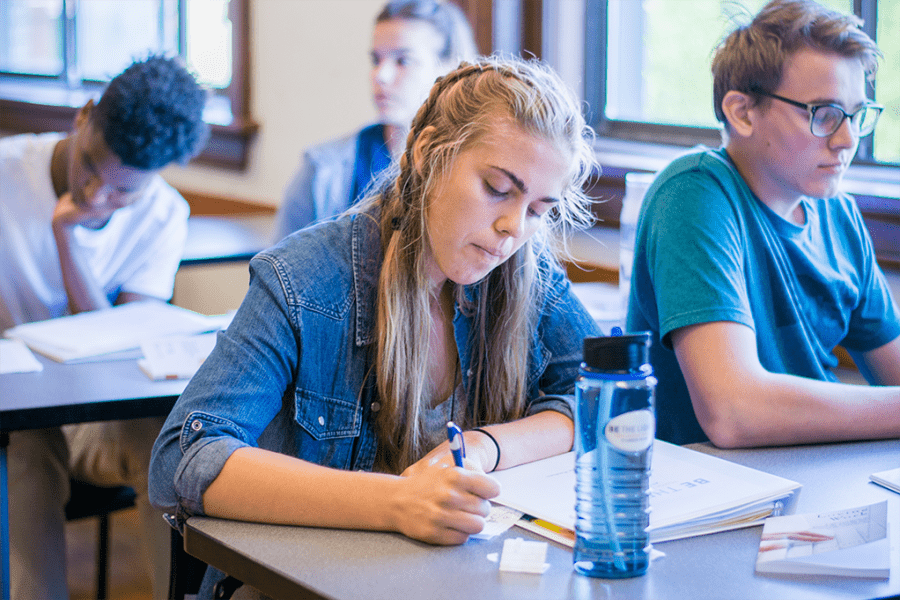 a student in a college classroom writing notes in a notebook next to another student