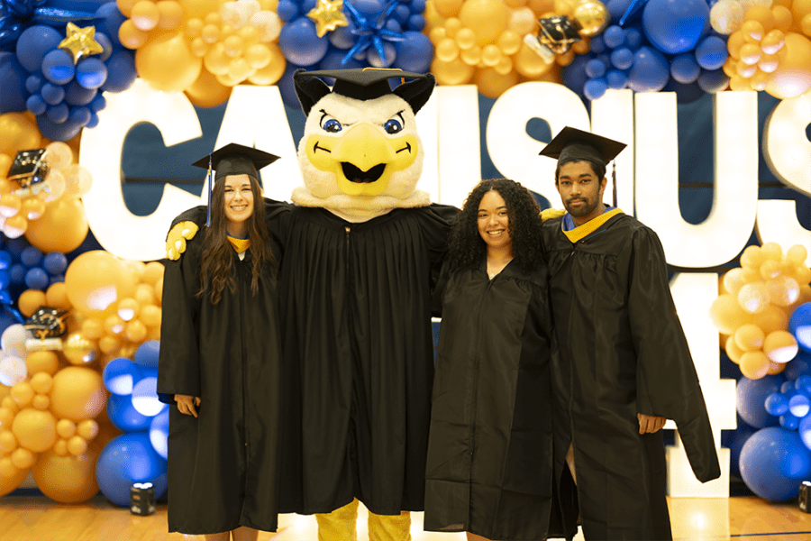 college graduates in cap and gown posing next to the school griffin mascot