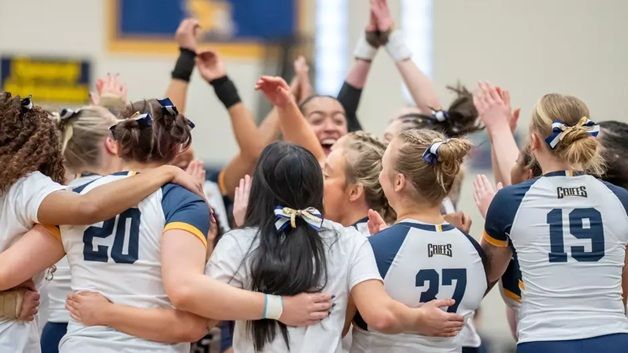 Group photo of the inaugural women's acrobatics and tumbling team in a huddle cheering