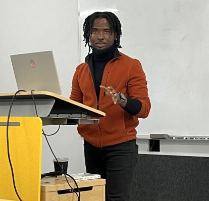 student presenting at a podium with a laptop in front of a white board