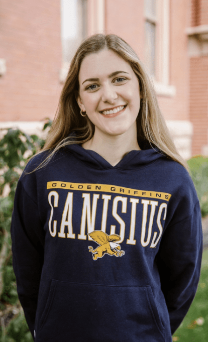 Student posing for photo in front of a college building wearing a Canisius sweater