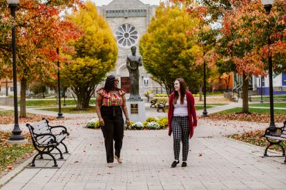 2 students in a college quad on a fall day with leaves around them, walking down a main path