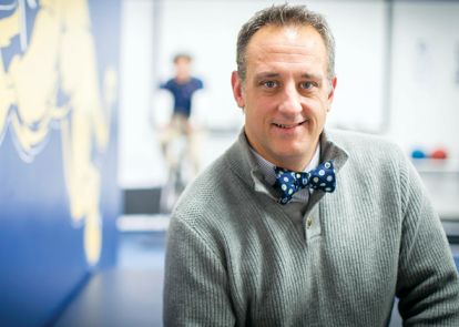 professor posing for a headshot near a wall at a college comments